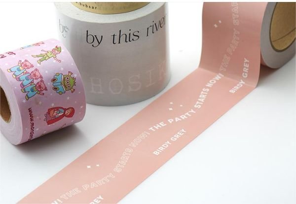 Three rolls of custom packaging tape: one with colorful cartoon characters, one with the text 'by this river,' and one pink tape with white text 'THE PARTY STARTS NOW' and 'BIRDY GREY.