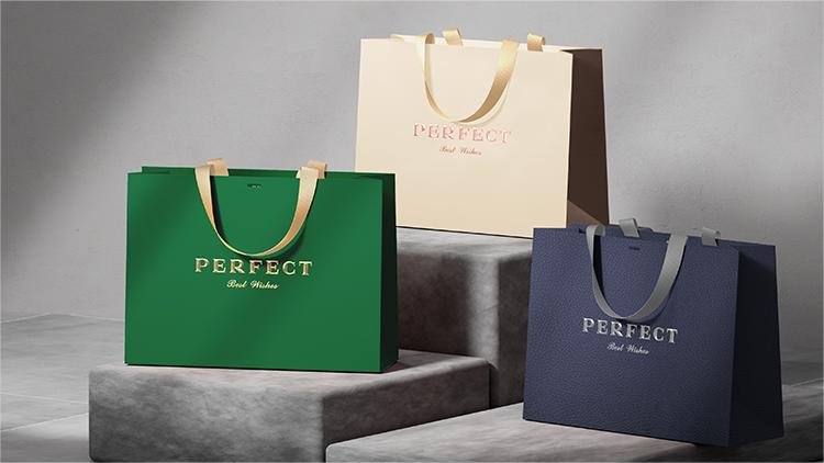 Three luxury paper gift bags in green, beige, and navy blue, each with the word "PERFECT" and "Best Wishes" printed on them, displayed on a tiered concrete platform.